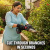 A woman wearing safety glasses and a light blue top uses a cordless chainsaw to trim green garden bushes. The text overlay at the bottom reads 'CUT THROUGH BRANCHES IN SECONDS'.